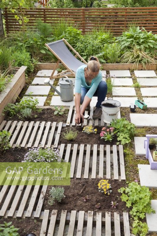 Woman creating drought tolerant flowerbed on the roof of garage. The flower bed is separated by slats, which are decorative and at the same time serve as a path. Adding layer of compost.