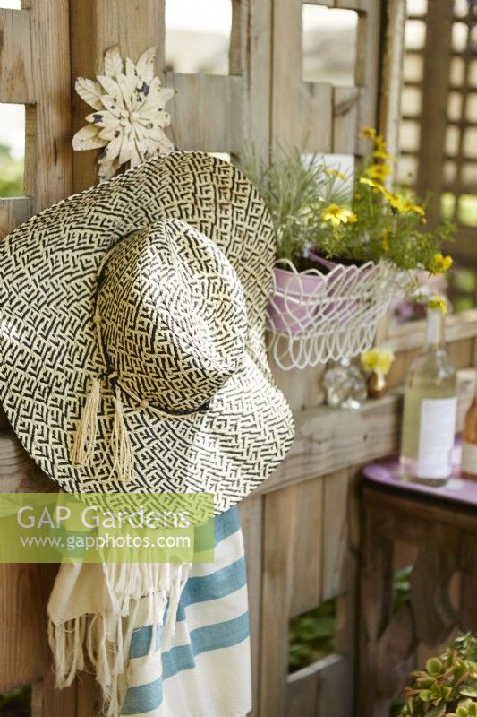 Sun hat and striped towel hanging from decorative hook on wooden trellis.