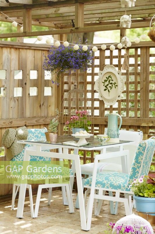 Vintage painted table and chairs on patio under a wooden pergola surrounded by trellis.