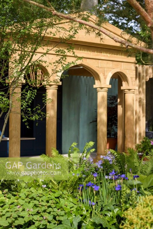 Borders with Irises, ferns Matteuccia struthiopteris and Geranium by the pavilion structure at The RNLI Garden, RHS Chelsea Flower Show 2022, Gold Medal. Designer Chris Bradshaw
