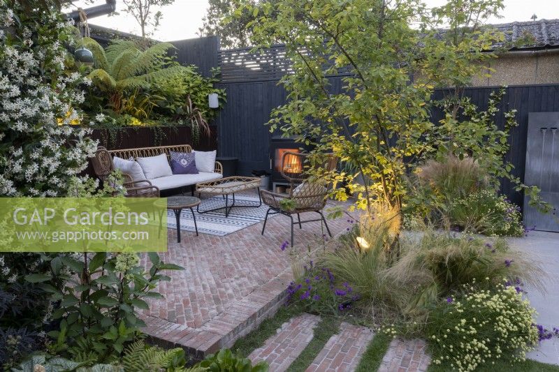 Patio area in suburban garden at sunset with lighting, seating and log burner