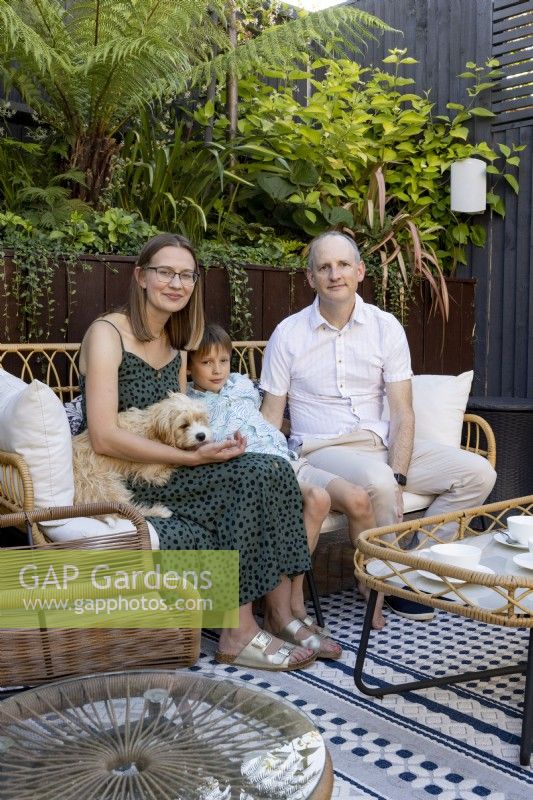 Family sitting on chair with dog in shady patio area in suburban garden
