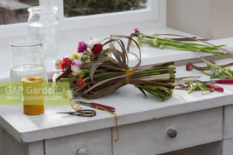 Tied spring bouquet of ranunculus and dried stalks of Chinese reed lies on the work table