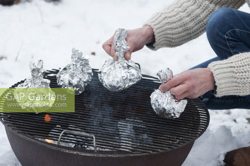 A woman placing potatoes in aluminum foil on the grill