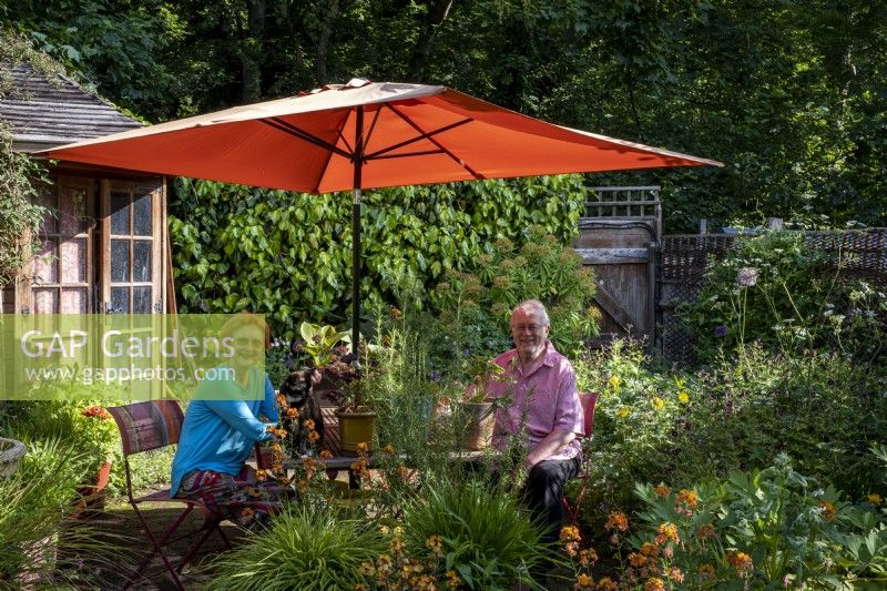 Garden owners sitting under parasol in a London cottage garden, summer