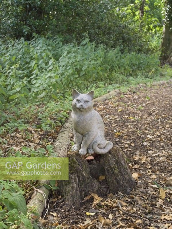 Ceramic cat sculpture sitting on  tree stump in woodland garden