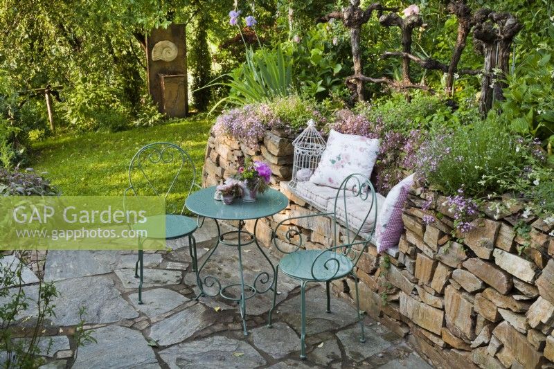 Stone paving patio with metal garden furniture and floral arrangement.