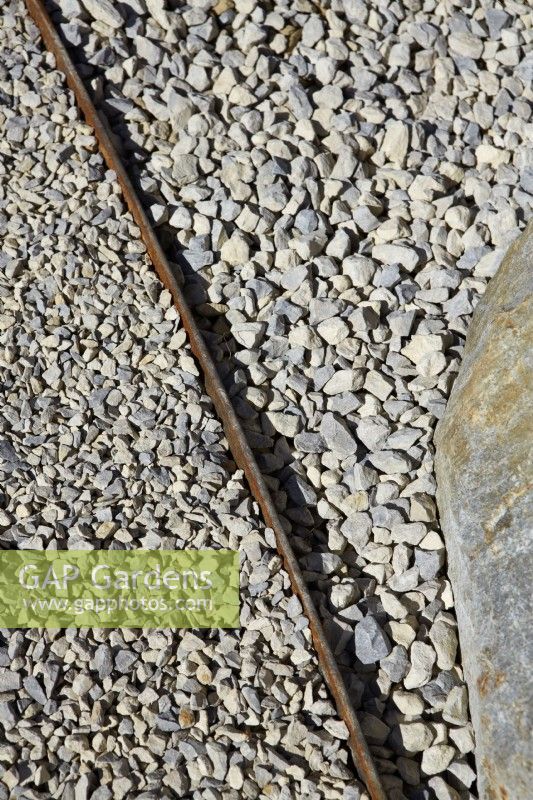 Rusted metal strip used as dividing detail on gravel pathway.