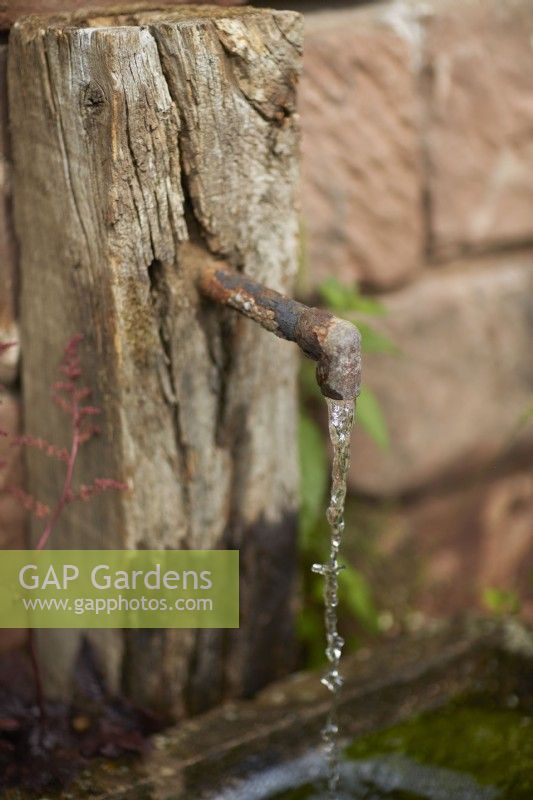 Water feature. Very old rusty iron water spout on old stone wall.