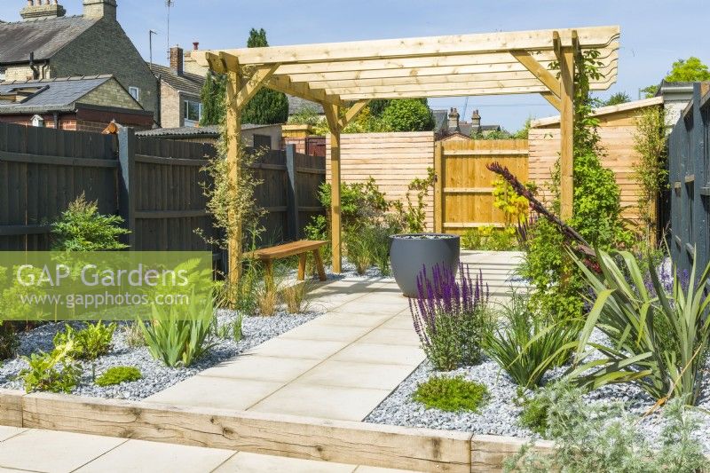Newly planted low maintenance town garden with paving, stone chippings and timber pergola to create shaded seating area. June
