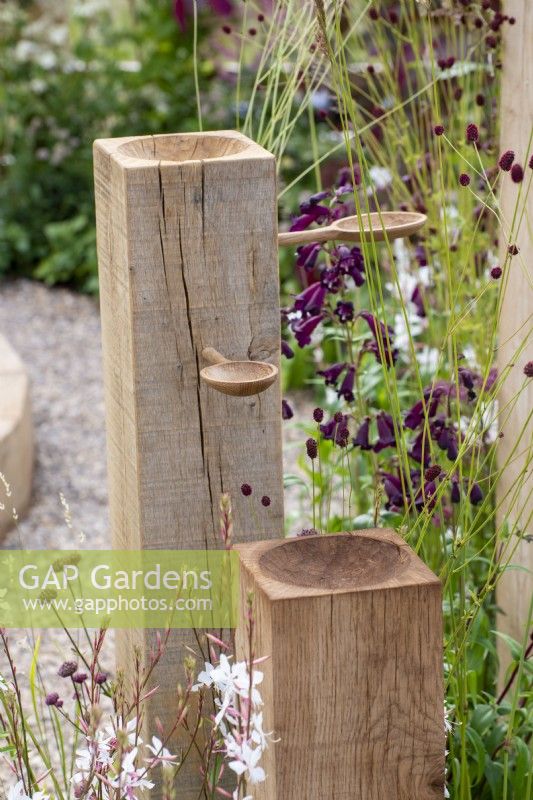 Bird feeder made with posts and wooden spoons, planting of Penstemon and Sanguisorba - The Wooden Spoon Garden - RHS Hampton Court Palace Garden Festival 2022