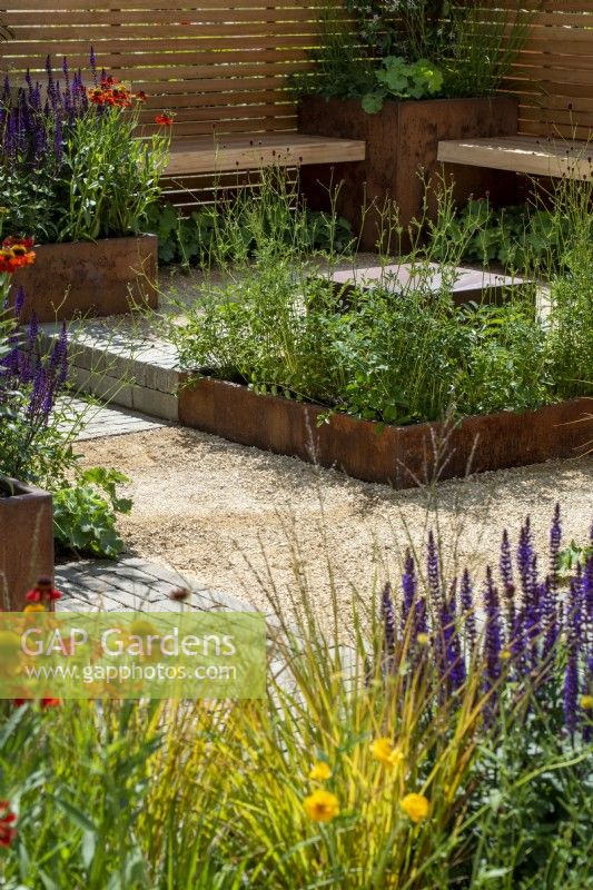 Seating area surrounded by wooden contemporary style fencing and Corten steel planters, hot planting includes Salvia 'Caradonna' and Helenium 'Moerheim Beauty' - The Lunch Break Garden, RHS Hampton Court Palace Garden Festival 2022