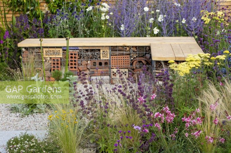 Insect hotel built into a wood and gabion bench surrounded by planting of Salvia 'Purple Rain', Gaura, Stipa tenuissima and Achillea 'Credo' - Turfed Out Garden, RHS Hampton Court Palace Garden Festival 2022