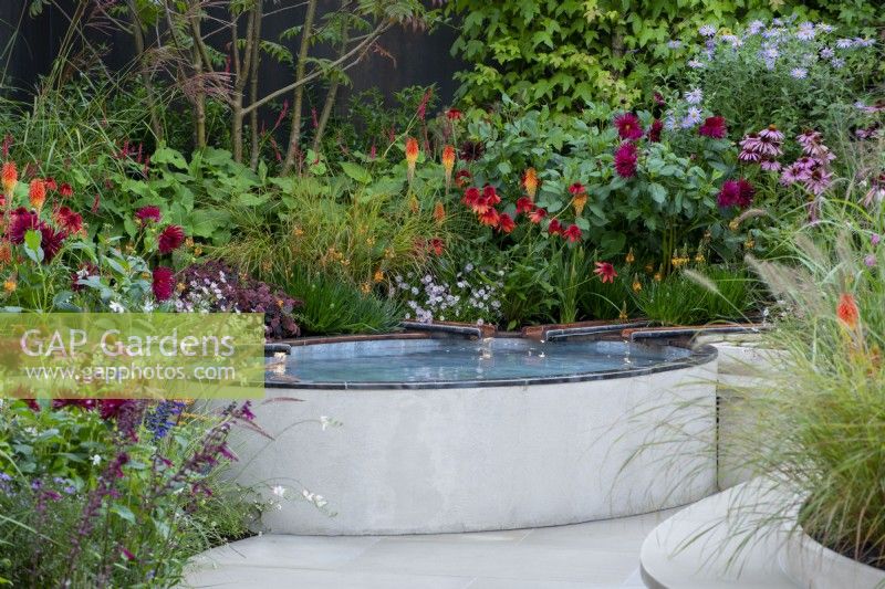 Copper water rills feeding into a raised pond with colourful planting behind, including Echinacea 'Eccentric', Persicaria amplexicaulis 'Firedance', Dahlia, Kniphofia and Echinacea purpurea - Finding Our Way: An NHS Tribute Garden, RHS Chelsea Flower Show 2021