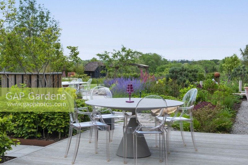 A raised deck overlooks borders of perennials and small trees.