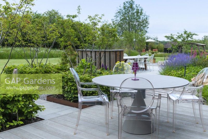 A raised deck overlooks borders of perennials and small trees. To left, raised square beds planted with multi-stemmed amelanchiers enclosed in low hornbeam hedges.