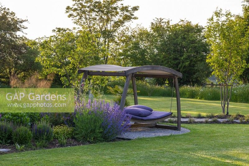 A swingseat is set into a border planted with a crab apple tree,  allium, salvia, geum and catmint.