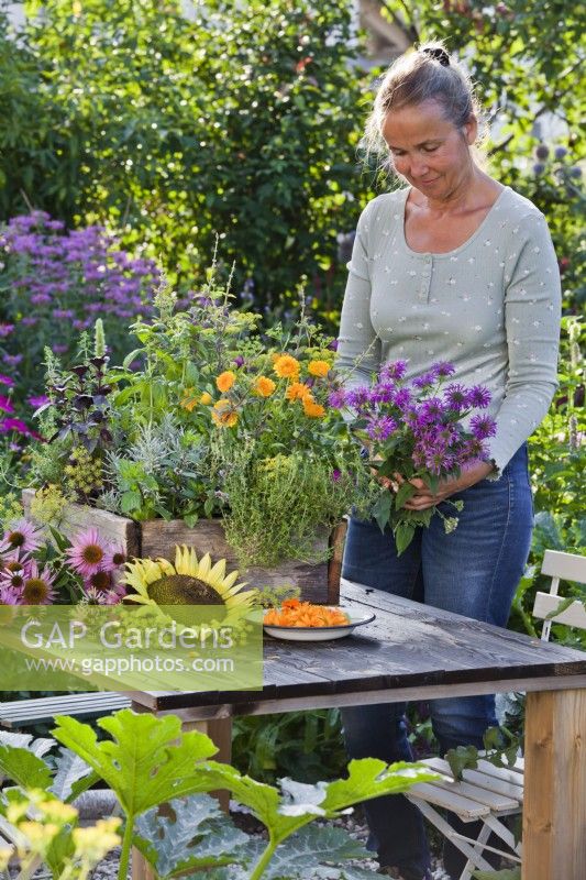Mixed herbs in a crate on the table and a woman holding a bouquet of monarda.