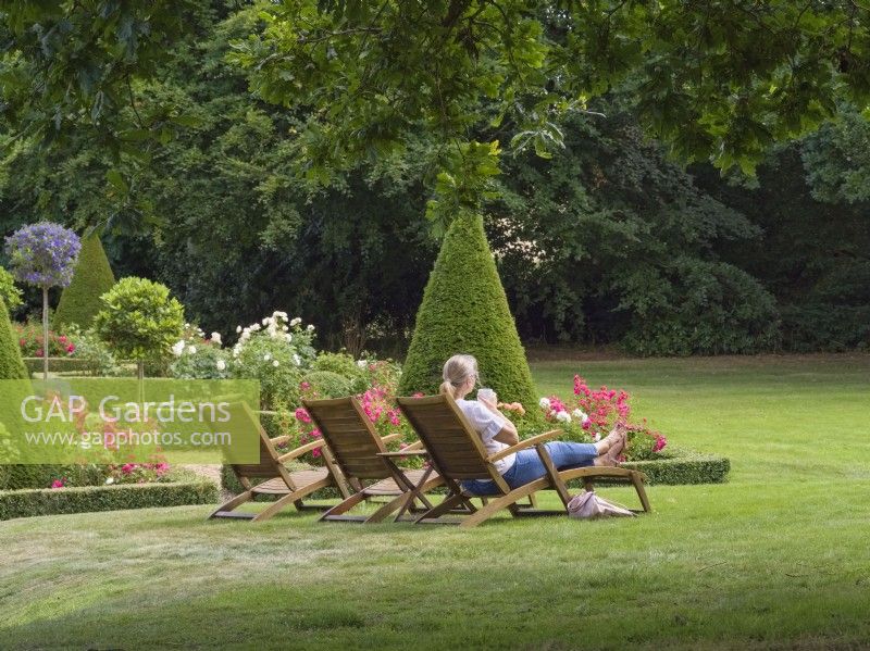 Woman relaxing on wooden sun lounger in Swafield Hall Gardens Norfolk