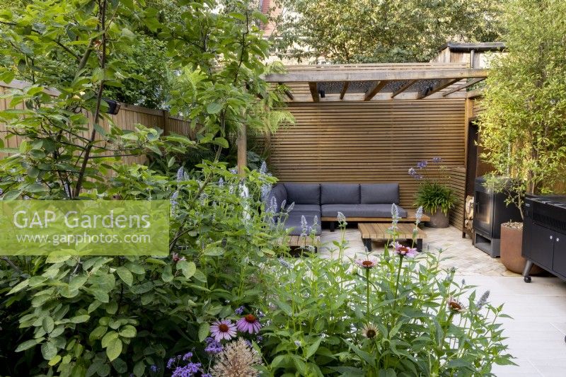 Looking across a herbaceous border towards patio area and contemporary wood pergola