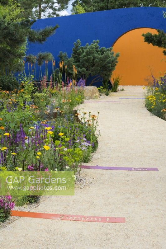 Colourful planting along curved path leading to circular opening  - Over The Wall Garden, supported by Takeda. RHS Hampton Court Palace Garden Festival 2022 