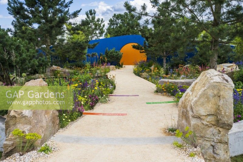 Colourful planting along curved path leading to' circular opening  - Over The Wall Garden, supported by Takeda. RHS Hampton Court Palace Garden Festival 2022 