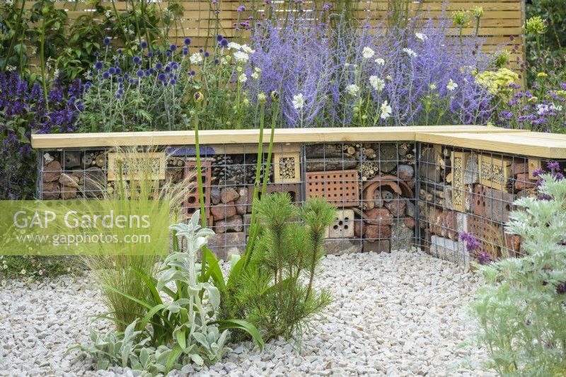 Bug or insect hotel inside gabion bench with wooden  top among  drought tolerant plants to attract pollinators, such as Salvia, Achillea, Echinops and  Perovskia - Turfed Out Garden, RHS Hampton Court Palace Garden Festival 2022
