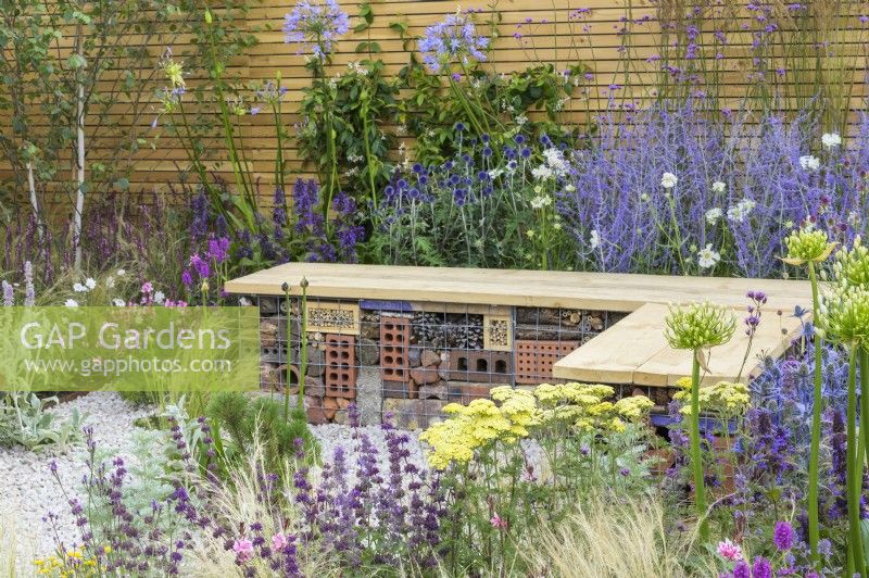 Bug hotel gabion bench with wooden  top in low maintenance gravel garden with drought tolerant plants to attract pollinators, such as Salvia, Achillea 'Credo', Agapanthus, Stachys byzantina and Stipa tenuissima -Turfed Out, RHS Hampton Court Palace Garden Festival 2022