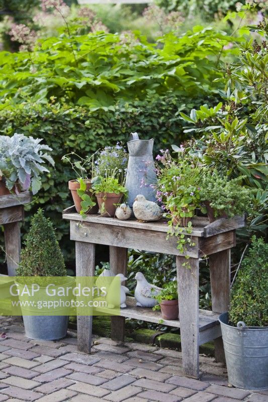 Outdoor arrangement on wooden table with potted plants, tools and dove sculptures.