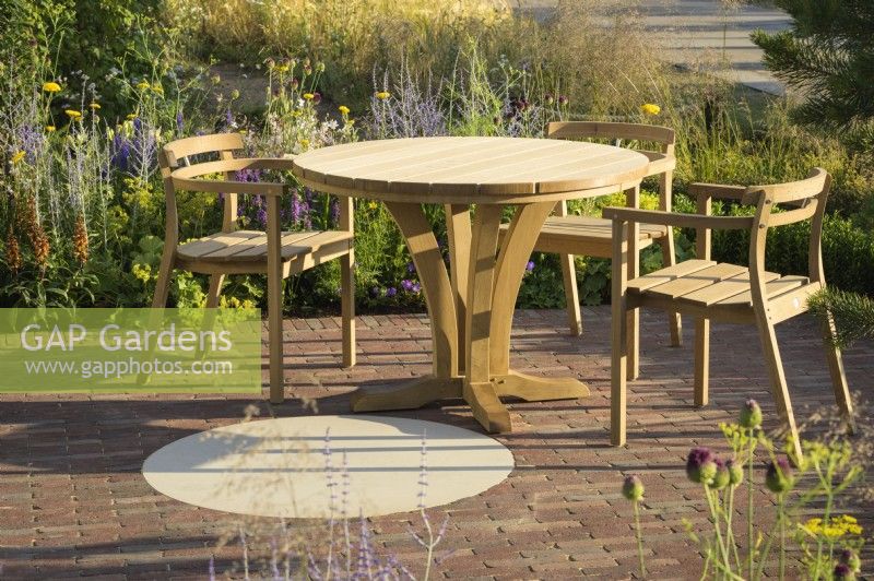 Sitting area with wooden table and chairs and Joy club garden - RHS Hampton Court Palace Garden Festival 2022