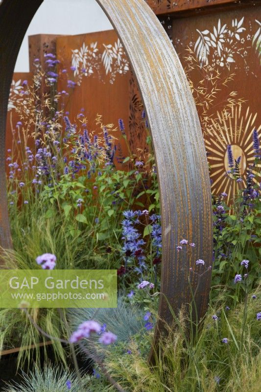 Corten steel garden feature and backdrop panels with mixed colourful planting. The Sunburst Garden. Design: Charlie Bloom and Simon Webster. RHS Hampton Court Garden Festival 2022.