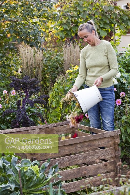 Woman adding waste from the garden to a compost bin.
