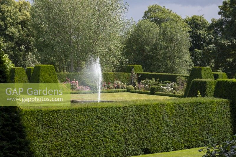 A fountain surrounded by Taxus baccata hedge, herbaceous borders and lawn in the formal garden at Renishaw Hall and Gardens.