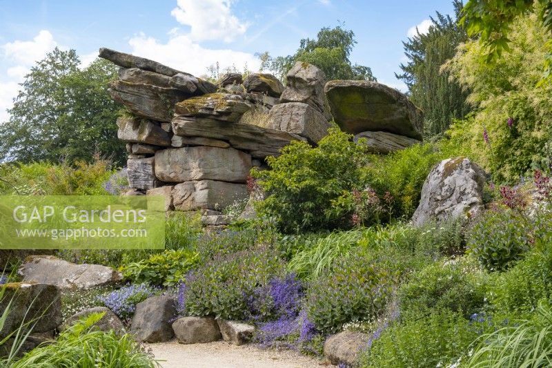 Naturalistic planting around dramatic rock formations in Paxton's Rock Garden, Chatsworth House and Garden.