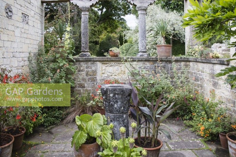 Small courtyard off the main steps to the terrace with plants in pots and central small stone font. July. Summer. 
