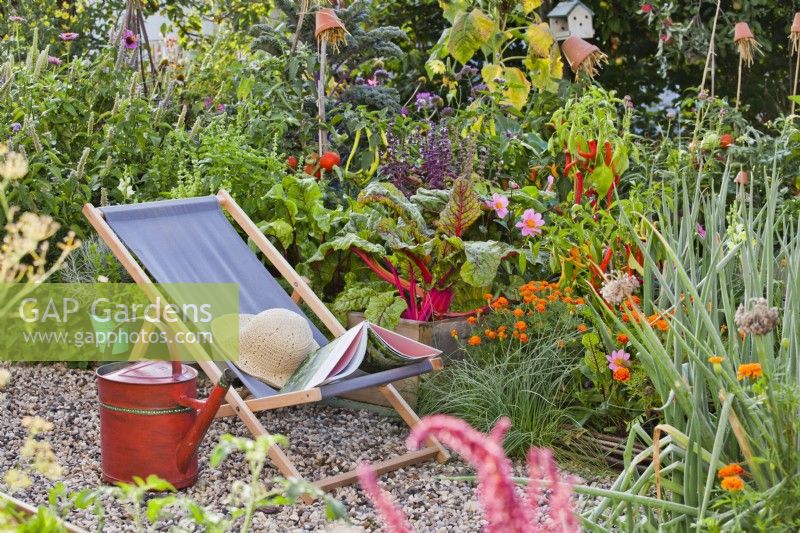 Deckchair on gravel and raised bed with growing crops in kitchen garden.