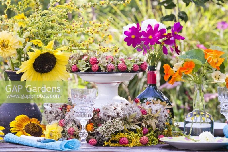 Outdoor dining table setting decorated with yellow, pink and orange themed bouquets in vases including sunflower, solidago, cosmos and nasturtium.