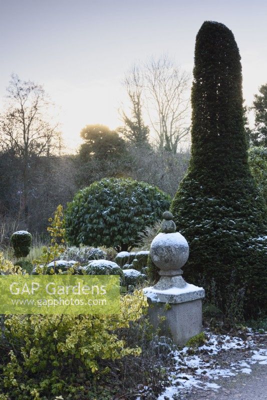 Finial dusted with snow in a formal garden in December, amongst clipped evergreens including yew and box.