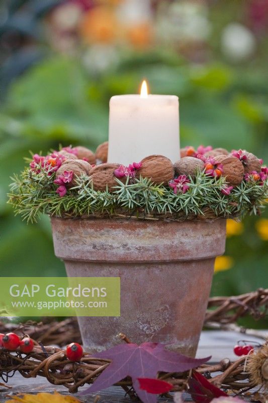 Terracotta pot with candle decorated with wreath made from walnuts, common juniper and spindle berries.