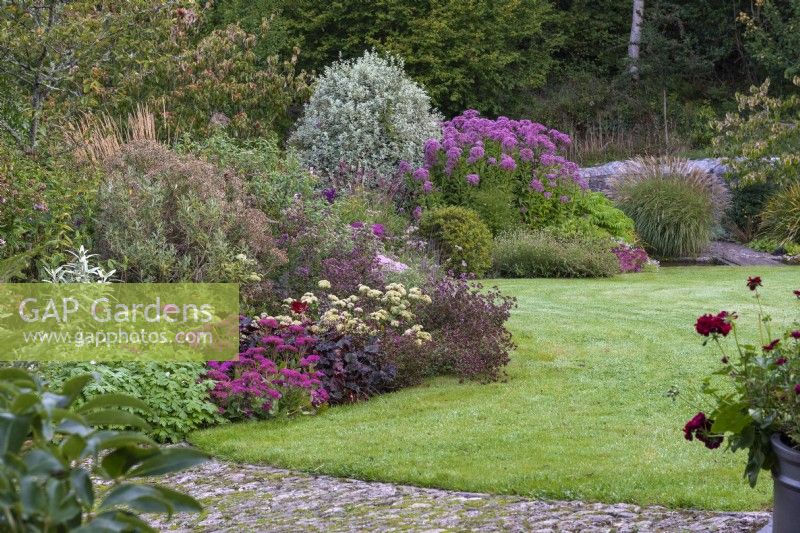 The stream garden with a meandering herbaceous border planted with miscanthus, pittosporum, and perennials such as sedums, hardy geraniums, heucheras, oregano and scabious.