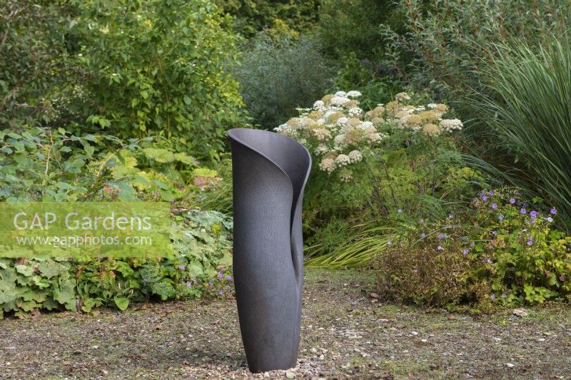 A sculptural pot by Adrian Bates rests in a woodland glade, edged in hardy geraniums and a clump of bullwort.