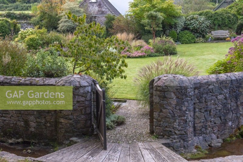 A gate opens into the stream garden, and the bridge and path passes between a miscanthus and dogwood to the lawn, at its centre a kidney-shaped bed of perennials and grasses.