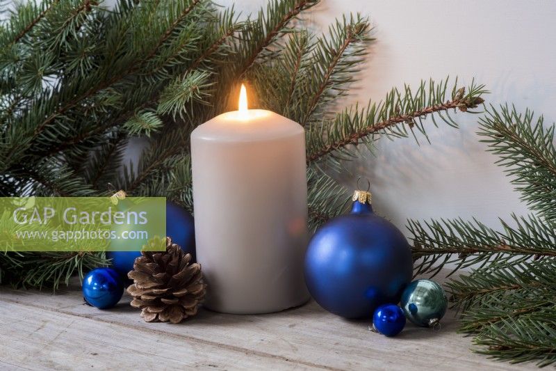 Grey pillar candle, blue baubles, cone and pine foliage again plain background