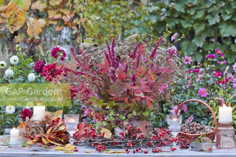 Autumnal arrangement on table including rose hip wreath and bouquet containing twigs with autumn leaves and late perennials.