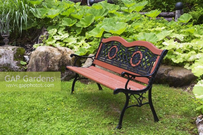 Antique brownish orange painted wood and black cast iron sitting bench in front yard garden in spring
