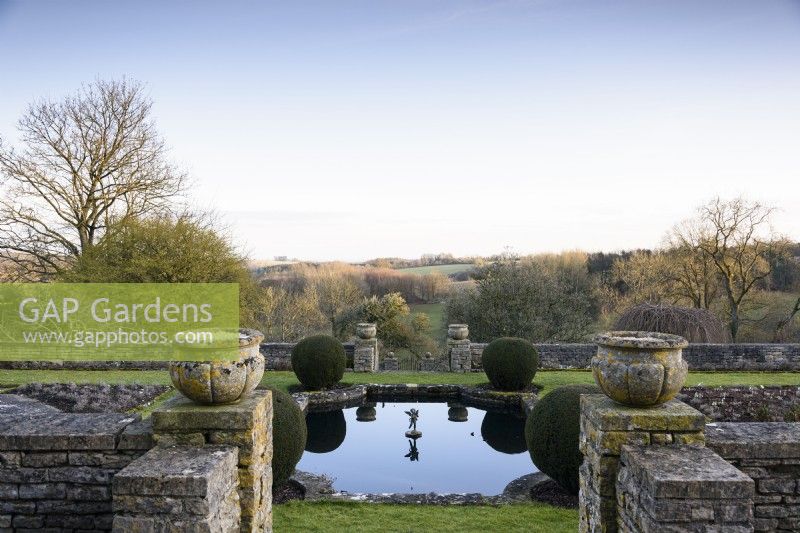 Rectangular lily pond on the Jewson Terrace at Cotswold Farm Gardens in February framed by clipped yew.