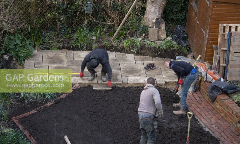 An overview of the makeover of a small London garden in progress including  a worker laying York Stone slabs for a terrace at the rear of the garden.
