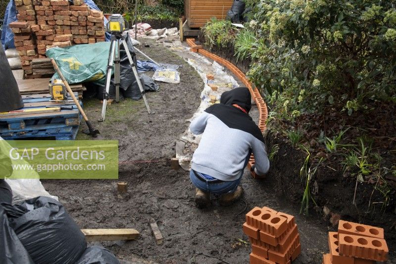 A worker building a low brick wall around a raised border during the makeover of a small London garden.