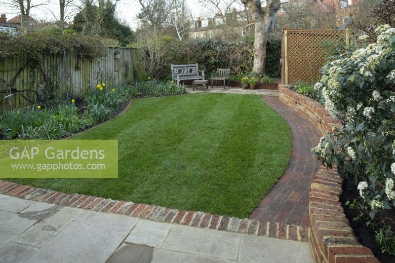 A London garden after a makeover with a new brick wall, path, extended terraces and newly laid turf.