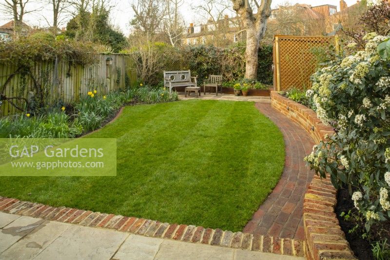 An 'After Photo' of a small London garden after a makeover which included a new low brick wall, curved path, extended terrace and newly laid turf.